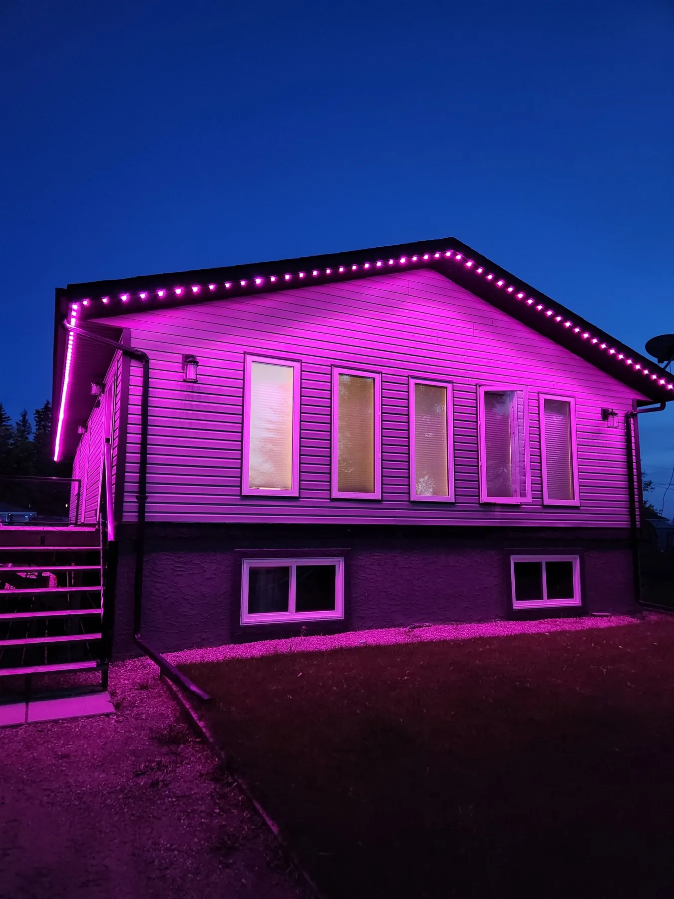 Magenta permanent LED lights along the gables of a stone and siding home