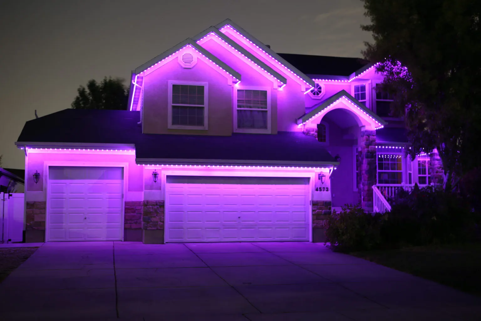 Purple permanent LED lights along the roofline and garage of a suburban home