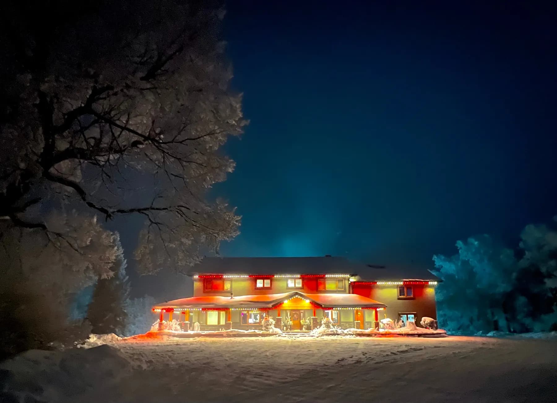 Long ranch home lit in warm white permanent lights with frosted trees at night